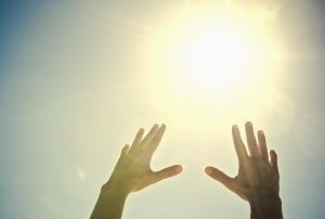 Mixed race woman's hands reaching toward sun