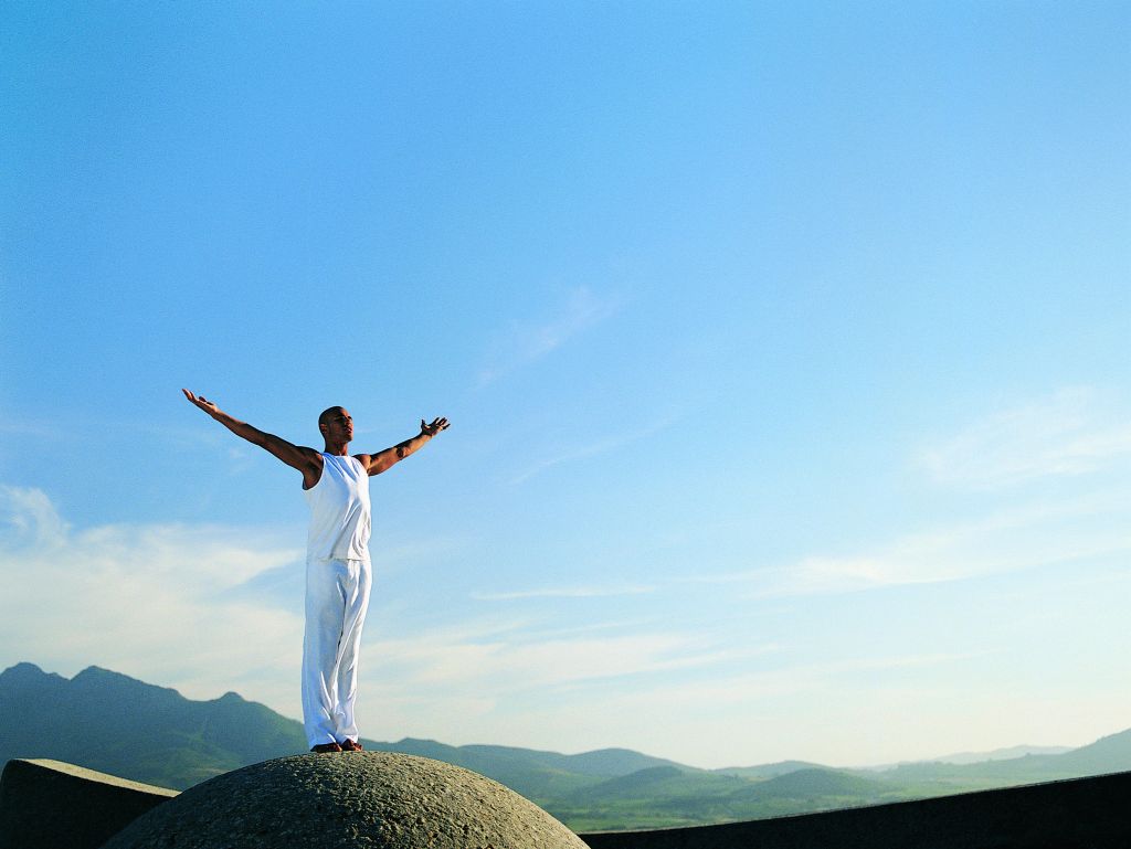 Man Standing on Boulder With Arms Outstretched