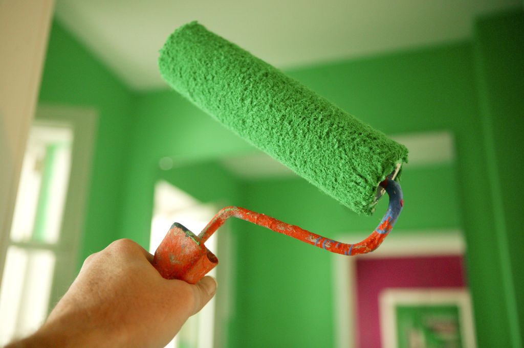 Man holding paint roller covered in green paint, close-up
