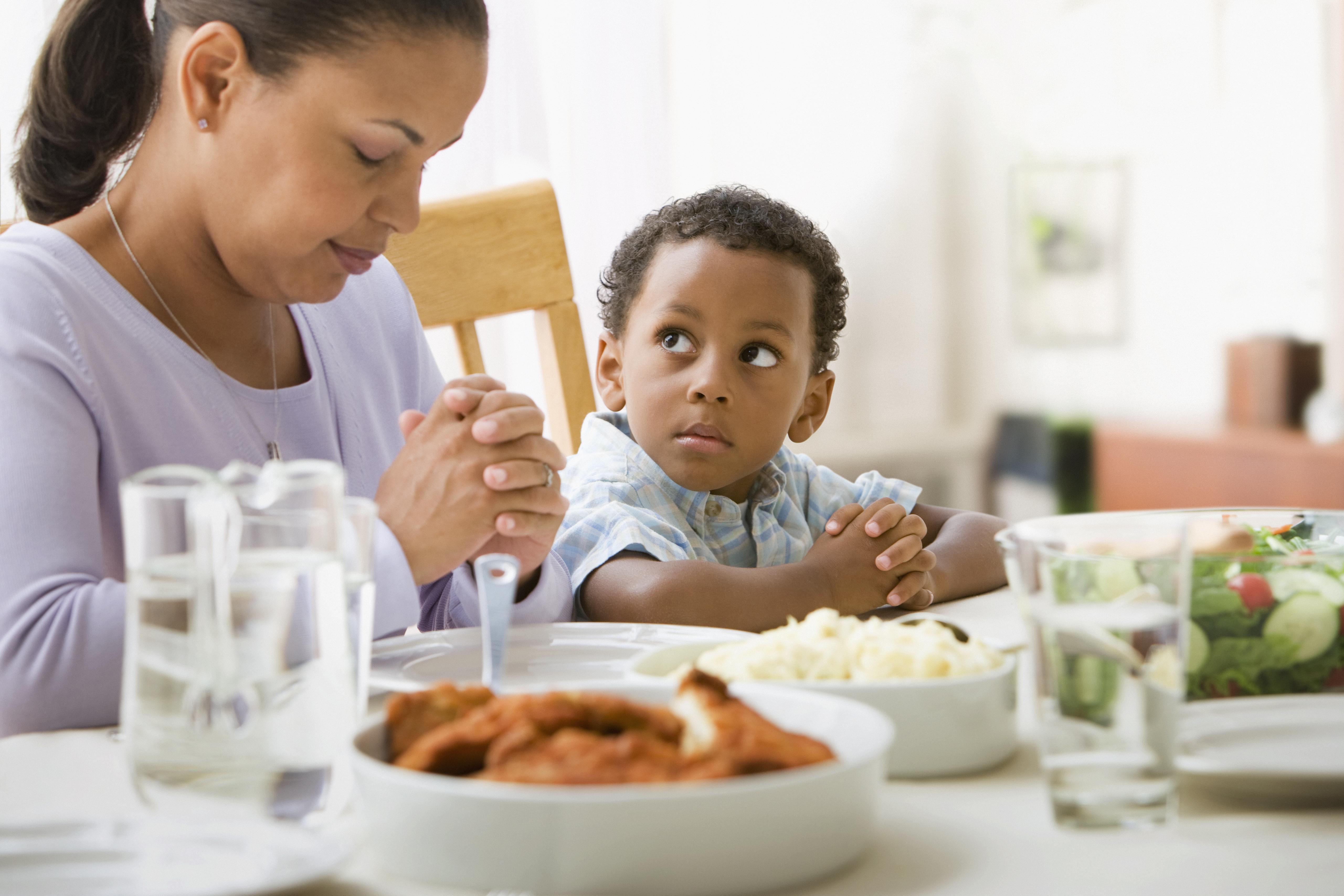 Mother giving thanks at the dinner table with son