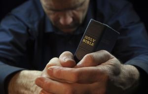 A Man praying holding a Holy Bible.