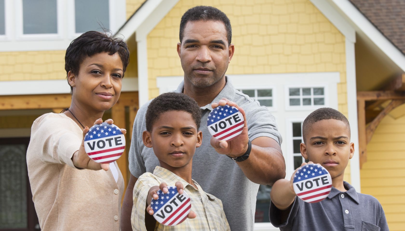 Black family holding Vote buttons outside home