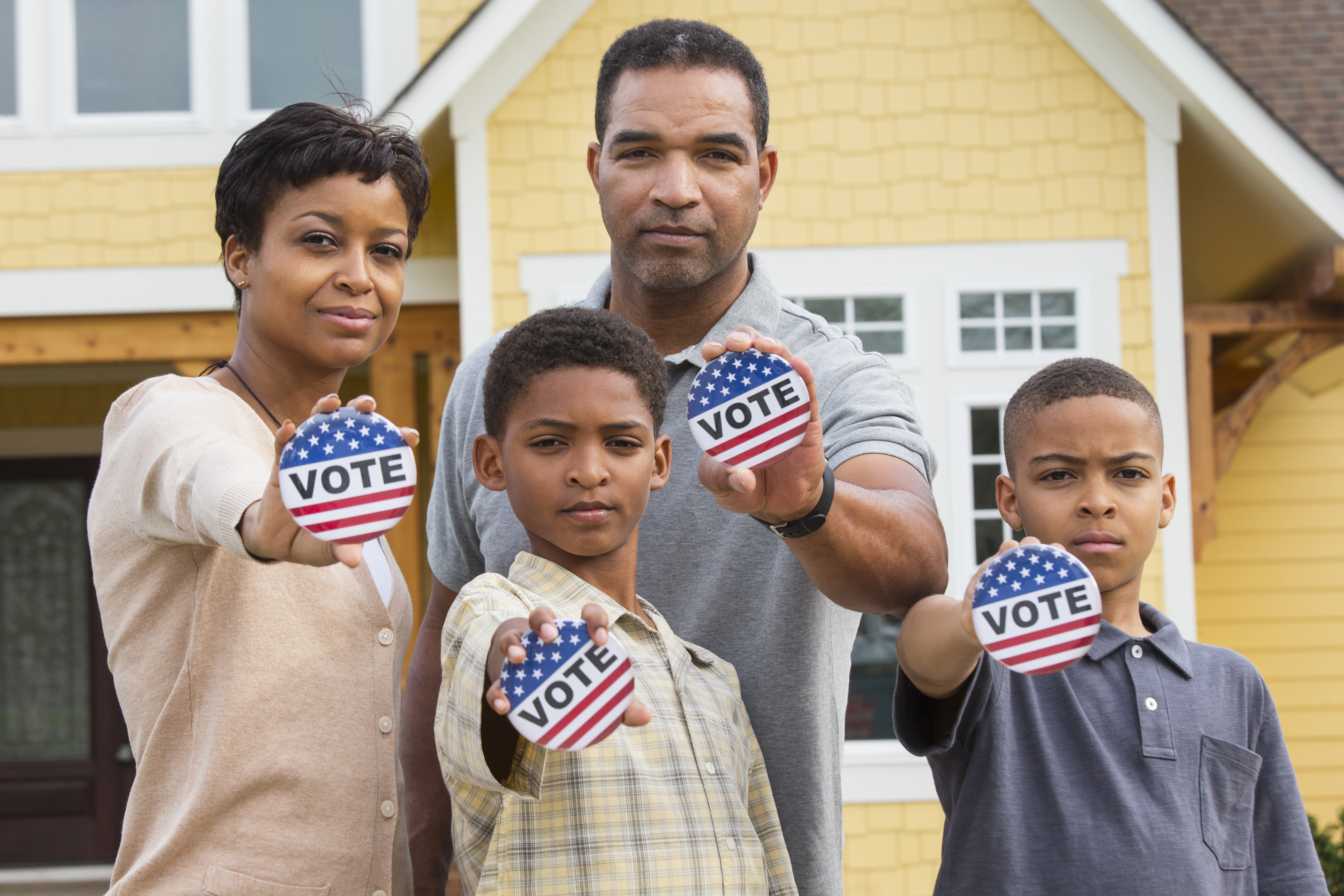 Black family holding Vote buttons outside home