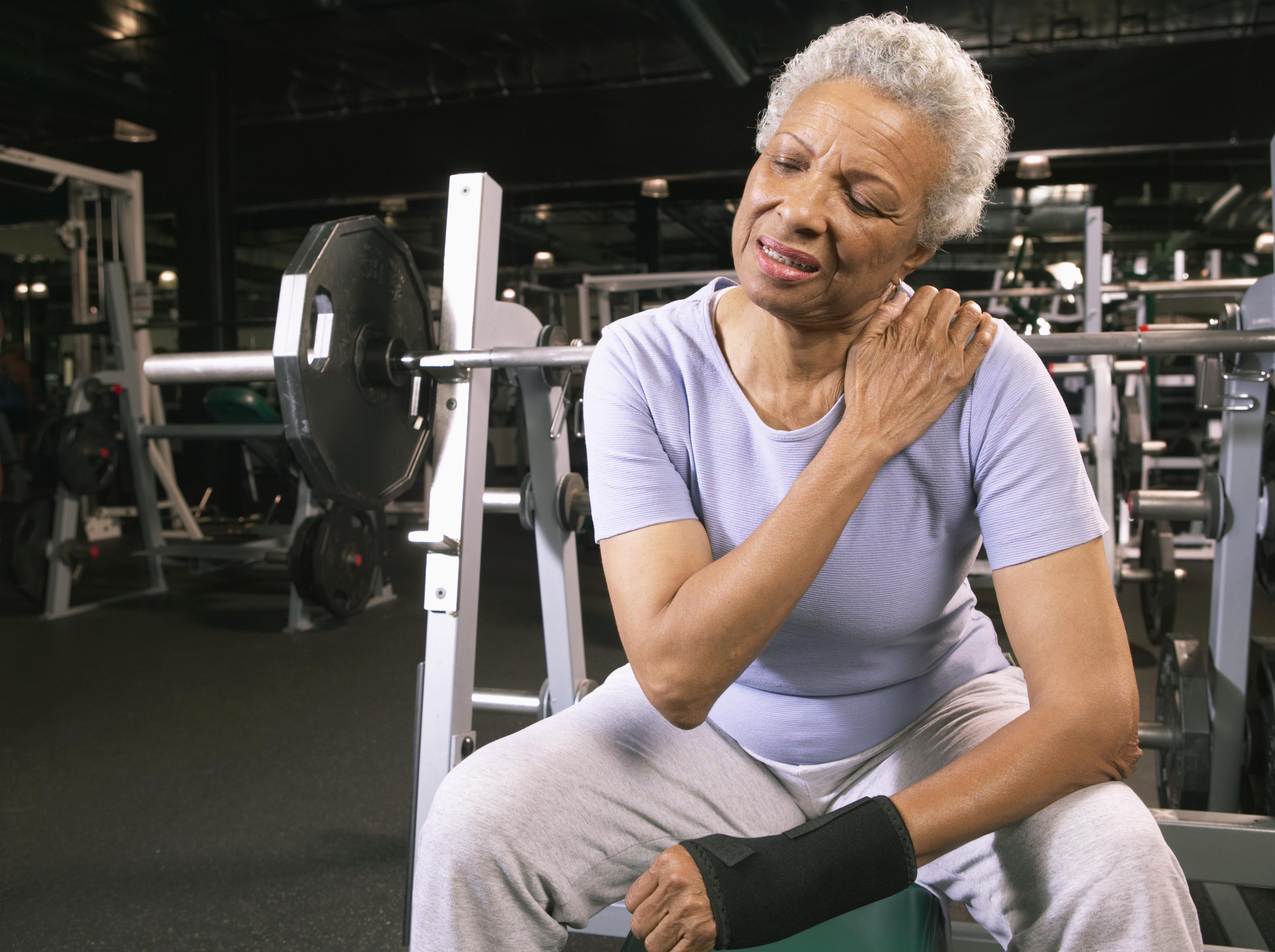 Senior woman in gym wearing wrist strap, rubbing shoulder