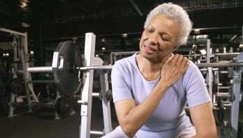 Senior woman in gym wearing wrist strap, rubbing shoulder