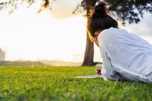 Rear View of Young Woman Lying on Chest over Green Grass on Sunset