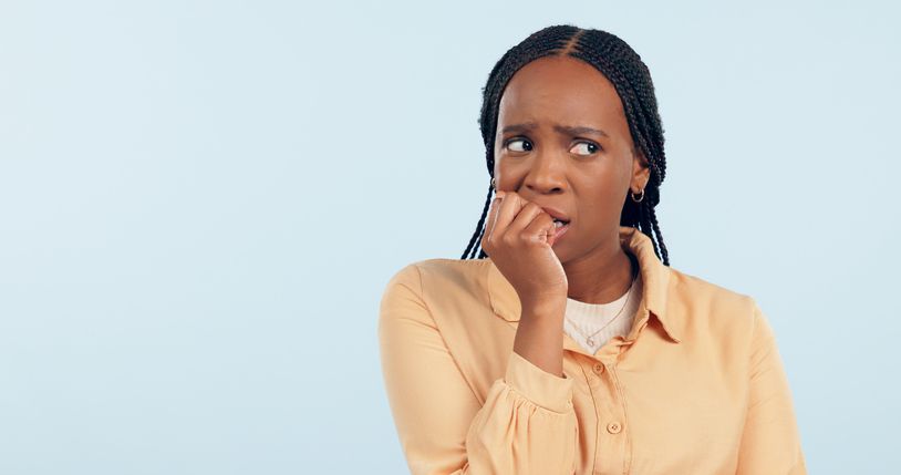 Woman, anxiety and biting nails in studio for stress, bad habit and thinking of horror on blue background. Nervous african model chewing fingers for terror, worry and scared of fear with mockup space