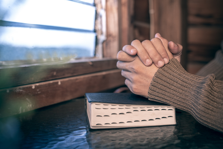 hands of man praying on bible at the window, christian background, devotional concept.