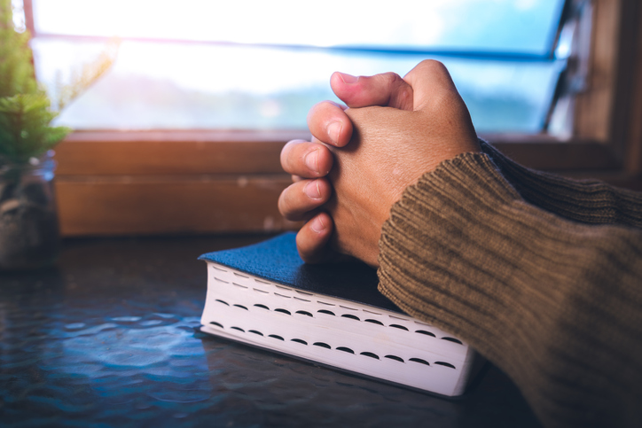 Close up of a man praying on bible at the window, christian background, devotional concept.