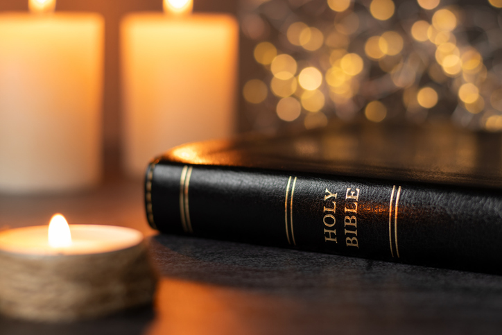 Holy bible book and candles burning with shiny bokeh background