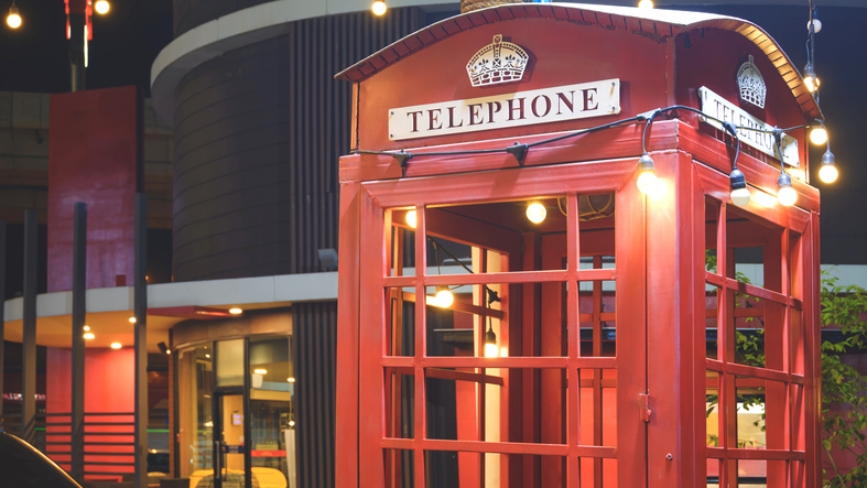Classic red vintage telephone booth decorated with warm string lights at night. Cinematic urban street photography with glowing bokeh background and iconic British style