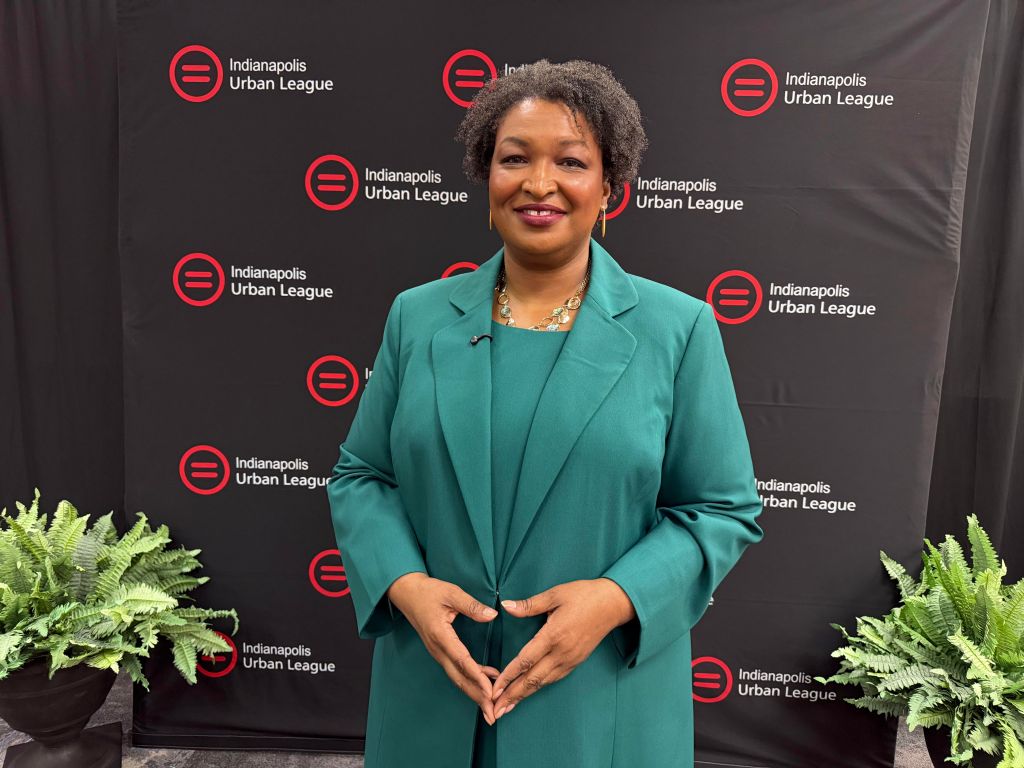 A smiling woman in a green coat standing in front of Indianapolis Urban League banners.