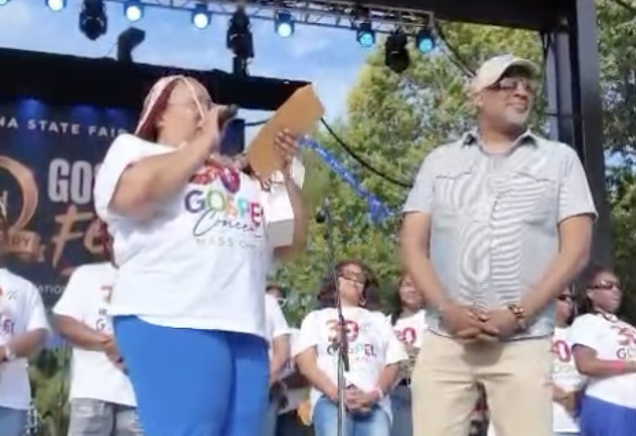 Two people on a stage at an outdoor event, one holding a sign that says "Go Canes" and the other wearing a white shirt.
