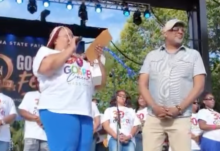 Two people on a stage at an outdoor event, one holding a sign that says "Go Canes" and the other wearing a white shirt.